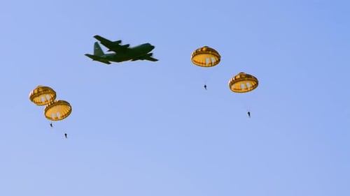Footage shows military paratroopers descending with parachutes from a drop plane in a sunny sky duri