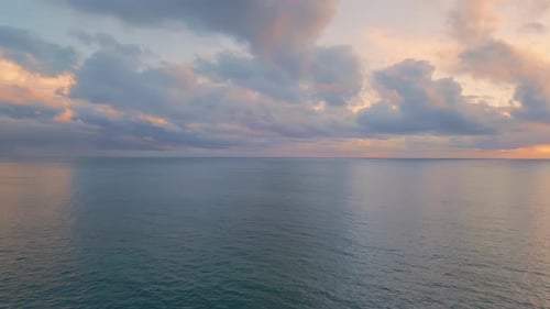 Golden sunlight breaks through grey clouds over tranquil deep blue ocean at sunrise