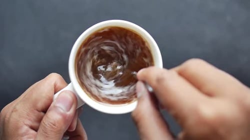 Cream Swirling Into Coffee in White Mug