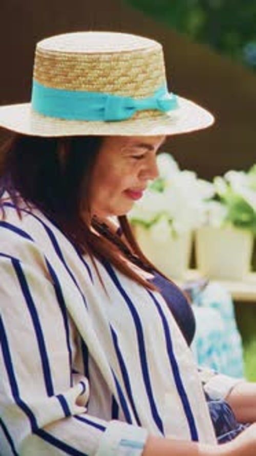 A Woman in a Stylish Straw Hat with a Blue Ribbon Enjoying a Relaxing Moment Outdoors Surrounded By