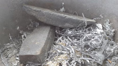 Hand pouring molten lead into a mold, with focus on the shimmering liquid metal, close up