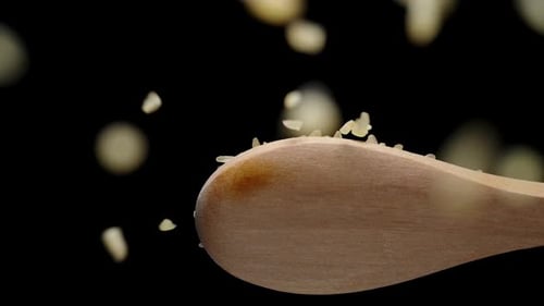 Brown bulgur grains fall down from a wooden spoon. Slow-motion.
