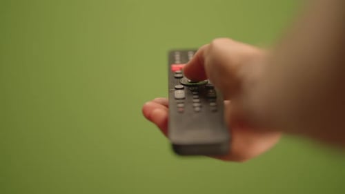 Una mano maneja un control remoto mientras está situado frente a una pared verde vibrante