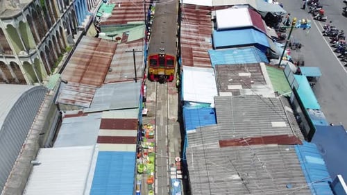 a drone shooting following a train and over the Mae Klong Railway Market (Hoop Rom Market) is a loca