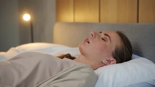 Couple hétérosexuel au lit, une femme dort et marque des points la bouche ouverte tandis qu'un homme fatigué est irrité