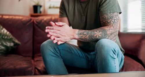 Tattooed Man Sits Calmly on Couch Rubbing Hands