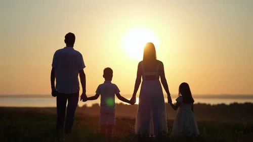 Family Looks at Sunset Raising Hands to Sky on Meadow