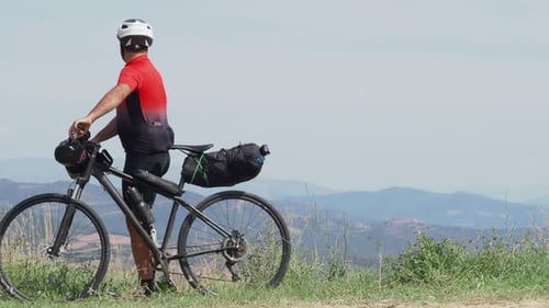 Cyclist with Bike Stands Atop Rolling Hills