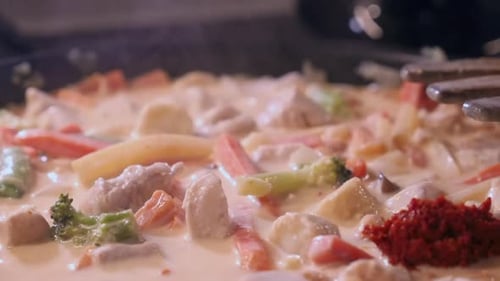 Curry paste added to creamy chicken, vegetables in steaming saucepan