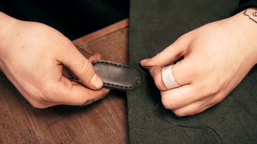 Close-up of the tailor's hands. The tailor sews a leather wallet. Leather product