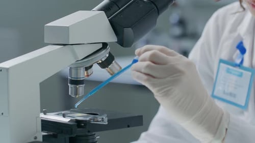 Chemist Pouring Blue Liquid on Microscope Slide in Scientific Laboratory