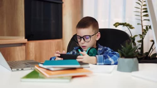 Young Boy Plays Game on Smartphone at Desk
