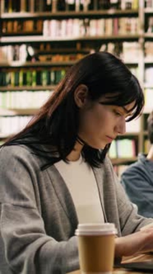 Vertical Video Young Adult Drinking Coffee and Taking Notes on Laptop From Open Book