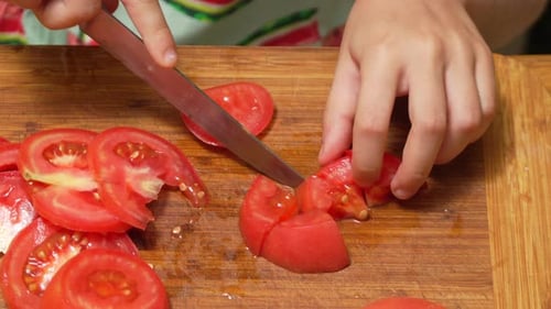 Child slicing red tomatoes on wooden cutting board