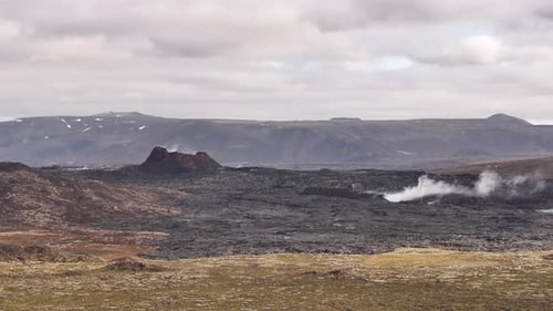 Vulkanlandschaft in Island mit dunklen Lavafeldern und geothermischem Dampf, der aus dem Boden aufsteigt.