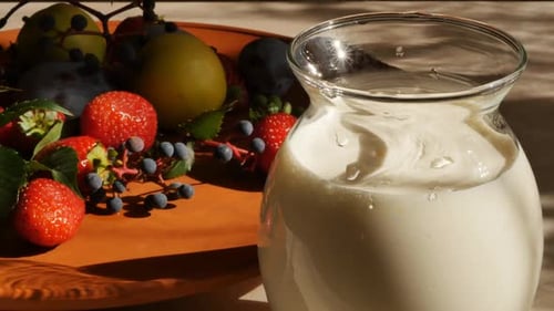 Dolly Shot of a Glass Jug with Creamy Yogurt Against the Background of Berries and Fruits Lying in a