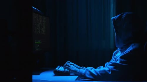 Hacker-Mann mit Kapuze tippt auf der Tastatur und bereitet sich darauf vor, ein Passwort zu knacken. Programmierer schreibt Code