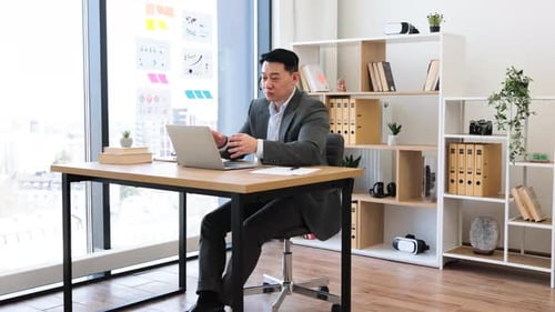 Asian Businessman Engaged in Online Video Call Wearing Headset in Office