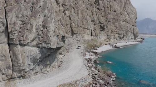Aerial View of a Car Driving Along a Winding Road Beside a Turquoise River in a Mountainous Region