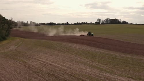 Aerial top view of tractor cutting furrows in farm field for sowing farm tractor with rotary harrow
