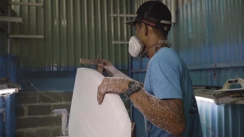 Man with respirator mask making home made DIY surfboard in workshop