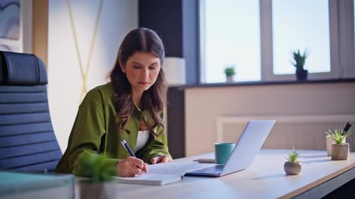 Corporate Worker Noting Information in Notebook Looking Laptop in Office Closeup