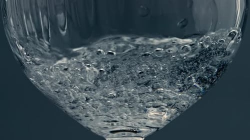 Closeup Water Pouring Glass at Dark Background. Splashing Fluid Filling Cup With