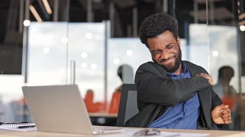 Tired Businessman Stretching Arms at Workplace in Modern Office