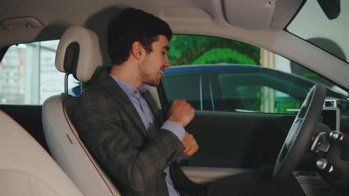 In a Stylish Showroom Filled with New Cars a Happy Guy Grooves to Music Behind the Wheel of His