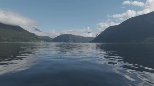 Slowmotion drone shot coming close to the water towards the Fjords in Norway on a sunny and cloudy d