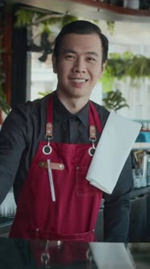 Male Bartender Cleaning Counter and Smiling at Camera