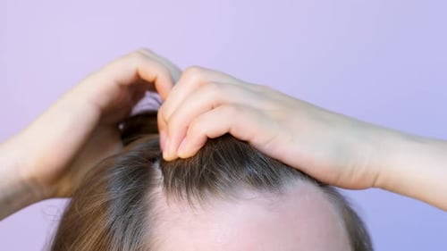 Girl touching her hair close-up on light pink background, hair loss concept.