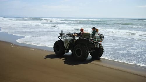 Traveling On Big Tire ATV On Shore Of Ocean Pair Of Tourists Admiring Seascape Extreme Tourism