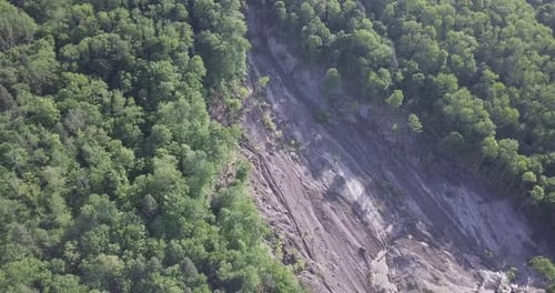 Glatt rotierende Luftdrohnenaufnahme eines großen, 20 Hektar großen Erdrutsches an einem steilen Waldhang, mit abgestürzten