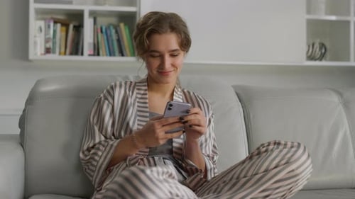Smiling woman using smartphone on sofa at home