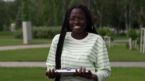 Smiling African American Woman Holding Books in Outdoor Park Setting Green Striped Shirt