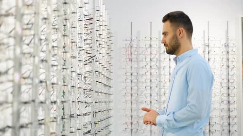 Side View of Male Customer Choosing Eyewear While Standing Near Shelf During Shopping at Optical