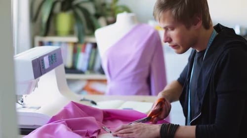 Young fashion designer at studio working with pattern cloth and scissors