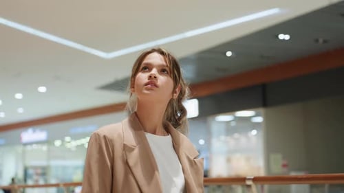 Closeup Woman Looking Up in Mall Under Angular Ceiling Lights Soft Blazer Silhouette and Thoughtful