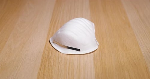 Men's hands lifting white protective mask on face and nose from wooden table on which lies protectio