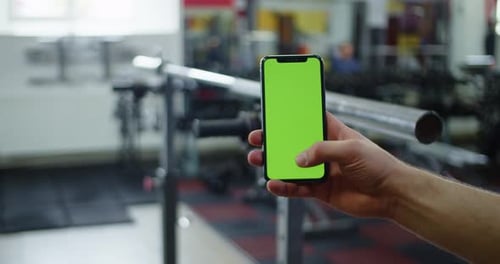 Male Hand Holding Smartphone in Gym Fitness App for Bodybuilding Green Screen