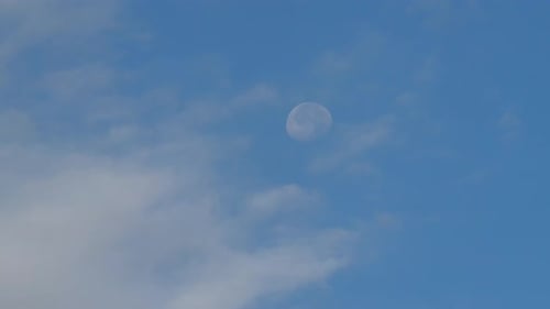 Bright moon in daytime blue sky with clouds