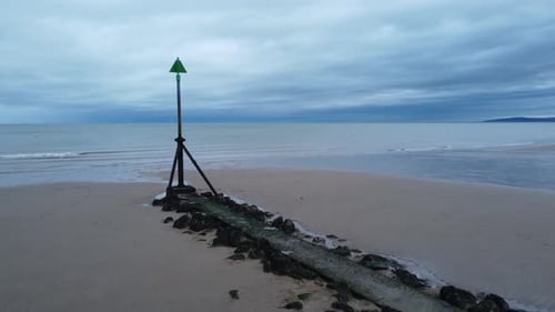 Coastal tide marker aerial view low slow push in right across moody overcast low tide seaside beach