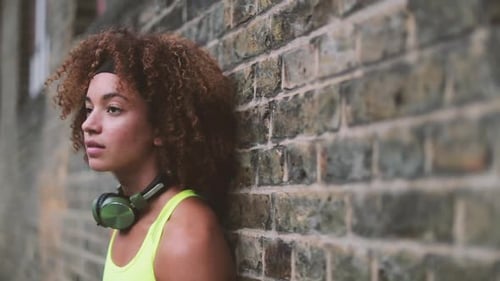 Athletic Woman Leaning Against Brick Wall with Headphones