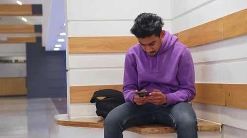 Asian man with short black hair uses smartphone indoors sitting in the corner