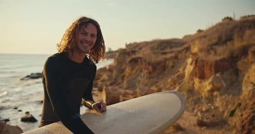 Portrait of a Young Guy with Curly Hair in a Black Wetsuit Who is Holding a Yellow Surfboard in His