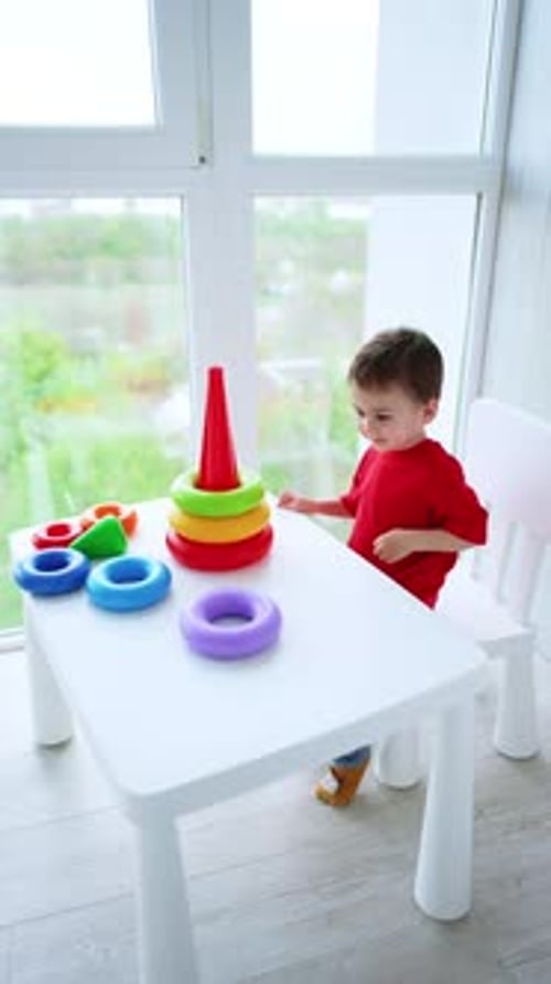 Un bebé feliz y sonriente sentado en el escritorio construye una pirámide. El niño pequeño aprende los colores y tamaños.