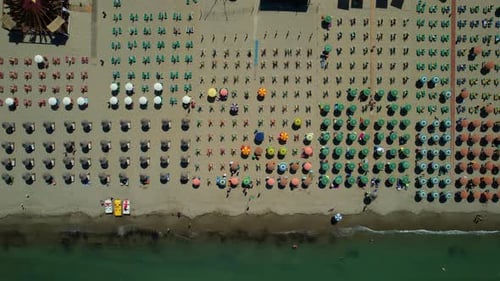 Aerial view of beach umbrellas in a row on the sandy beach kissed by the Adriatic Sea, creating a pi