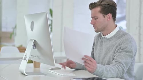 Serious Young Man doing Paperwork in Office
