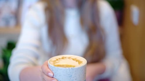 Woman drinking latte art coffee from ceramic cup in a cafe